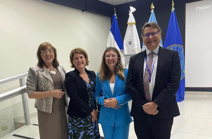 Silvia Belvisi junto a 3 participantes del evento. Al fondo 4 banderas, entre ellas, de El Salvador