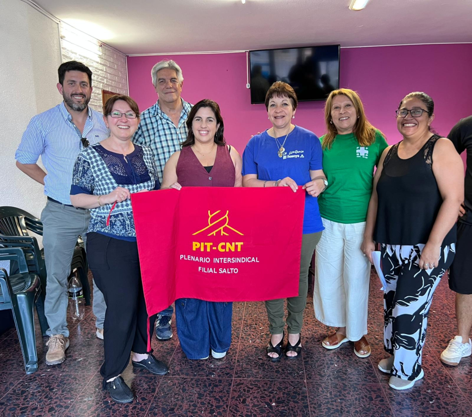 Puig y equipo con personas asistentes a la reunión y bandera de Pit-Cnt Salto