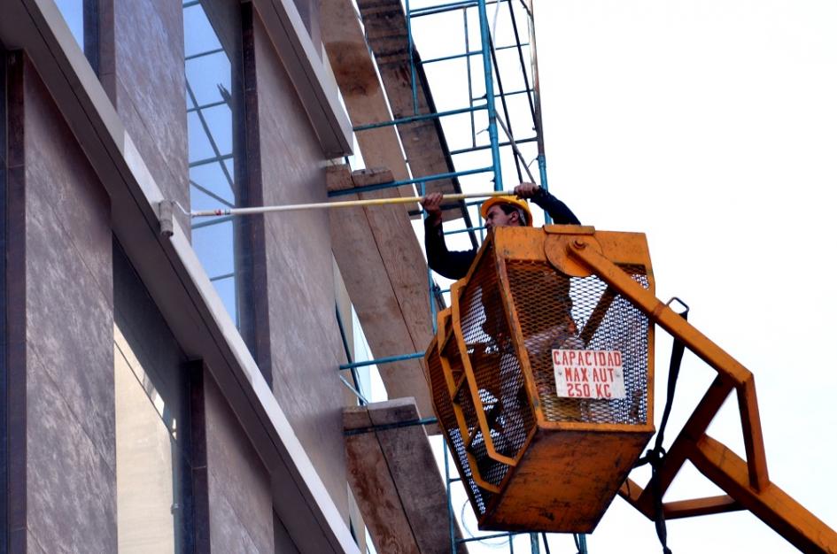 Hombre en grúa pintando fachada