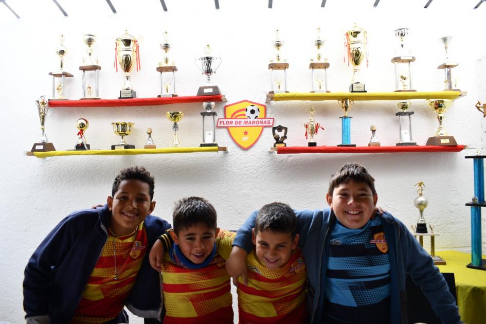 Niños del club de baby fútbol Flor de Maroñas, junto a trofeos deportivos