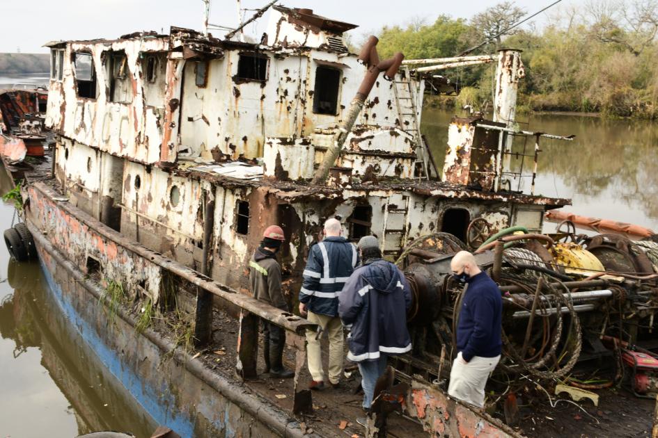 Avanza retiro de barcos abandonados en arroyo Las Vacas Ministro Olaizola y trabajadores caminan sobre embarcación en proceso de desguace