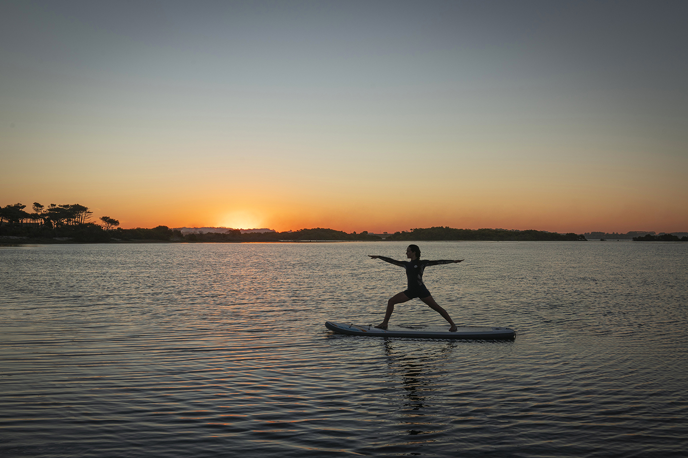 Mujer sobre una tabla de paddle surf en un río, haciendo yoga en un atardecer