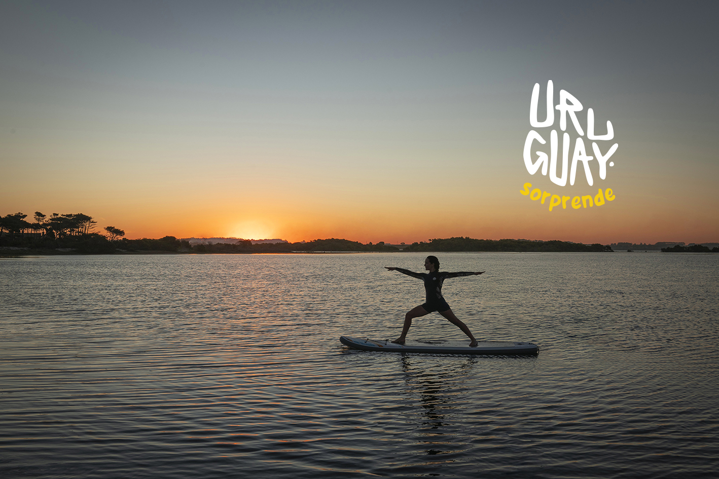 Mujer sobre una tabla de paddle surf en un río, haciendo yoga en un atardecer