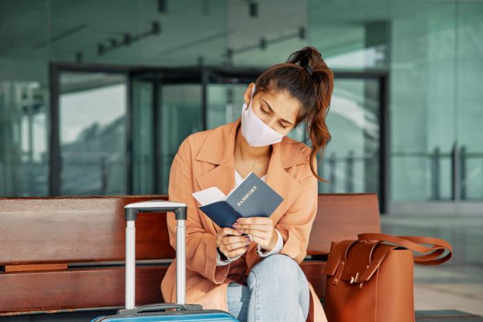 Pasajera con tapabocas revisa su pasaporte en aeropuerto durante la pandemia Pasajera con tapabocas revisa su pasaporte en aeropuerto durante la pandemia