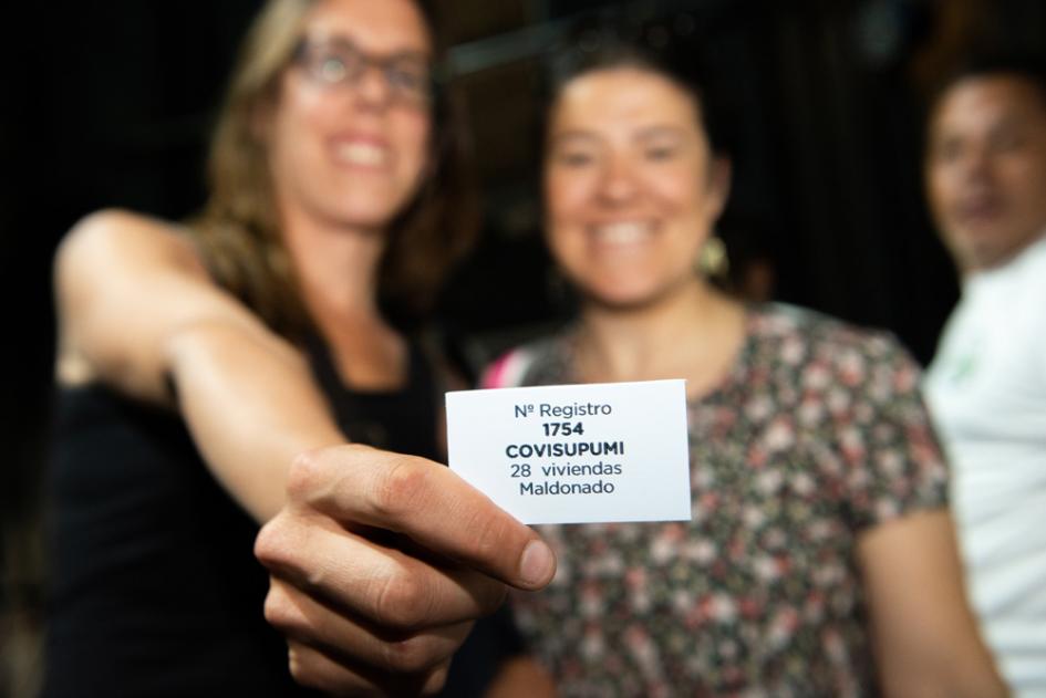 Mujeres con ficha de su cooperativa siendo sorteada Sorteo de coopertivas