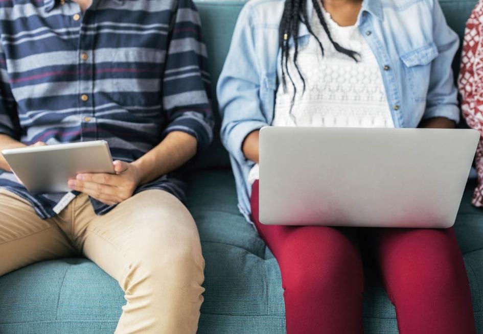 Se observa dos cuerpod de una adolescente y un adolescente sentados con su tablet y computadora. No se les ve la cara