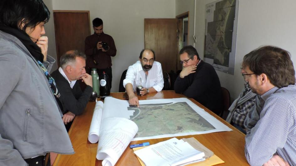 Imagwen de reunión de Freitas, Olivera y demás técnicos y técnica alrededor de una mesa observando un mapa