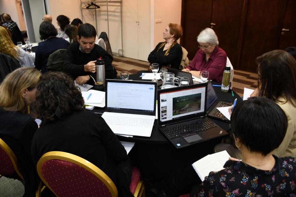 Participantes en la mesa intercambiando. Computadoras abiertas y documentos