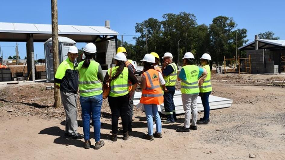 Autoridades y equipo técnico visitante parados en medio del predio donde se alojarán las viviendas temporales escuchando al representante de UPM II que guía la visita 