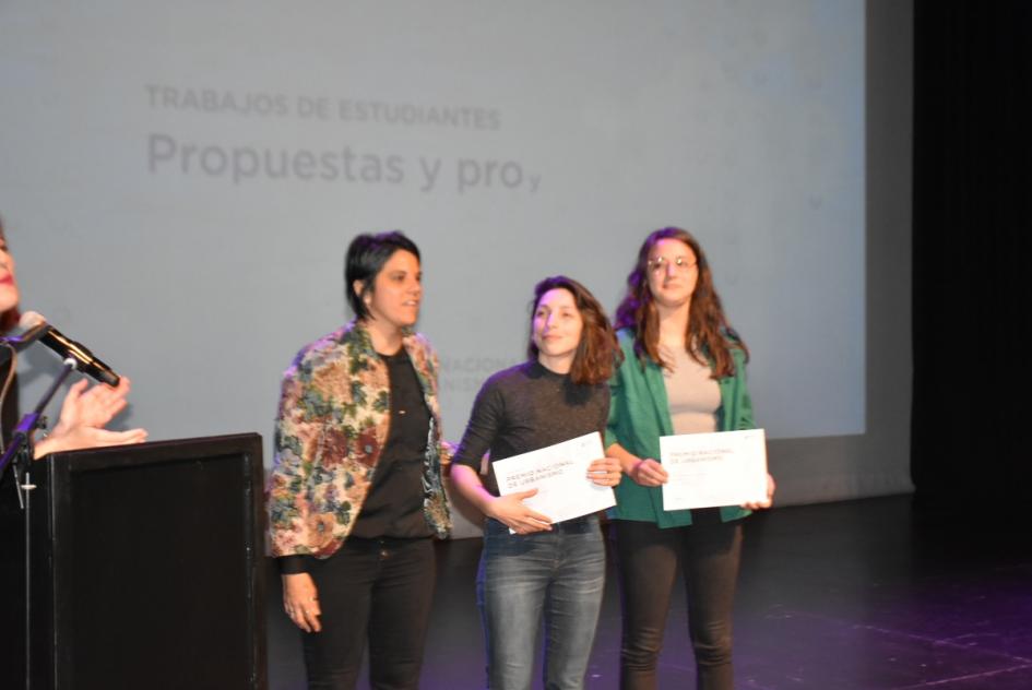 Una de las miembros del jurado y dos dos ganadoras posan para la foto en el escenario al momento de la entrega de sus certificados 