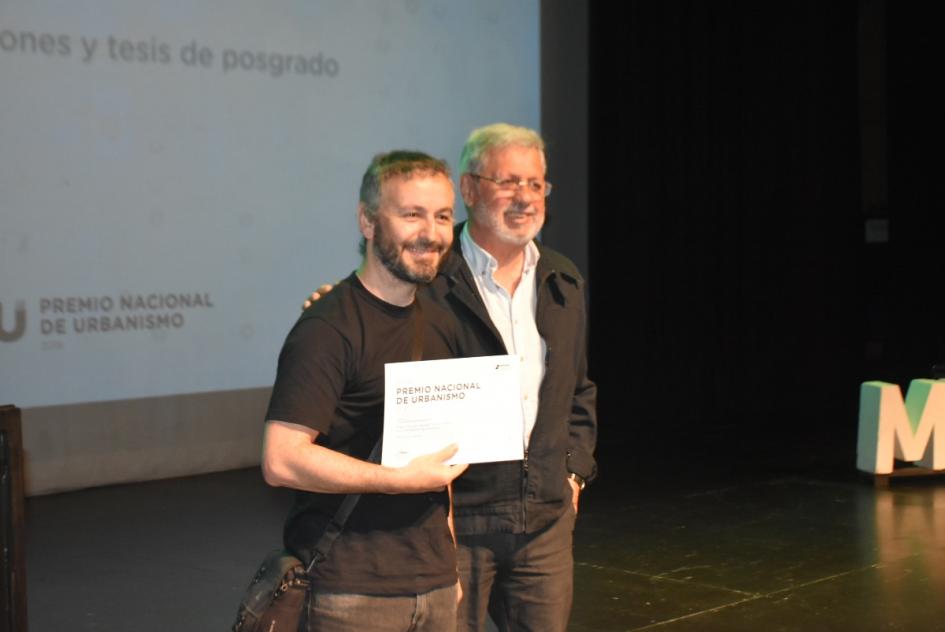 Miembro de jurado con uno de los ganadores en el escenario posan para la foto al momento de la entrega de certificado 