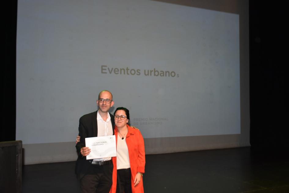 Ganador y una de las miembros del jurado posan abrazados para la foto en el escenario 