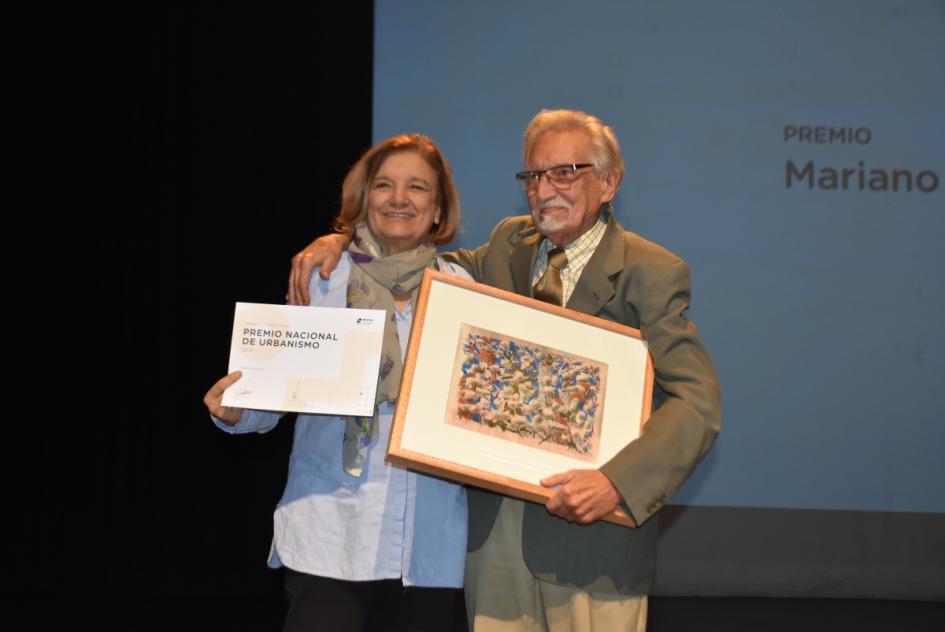 La ministra De León posa para la foto abrazada de Mariano Arana, él sosteniendo y mostrando la obra y ella mostrando el certificado 