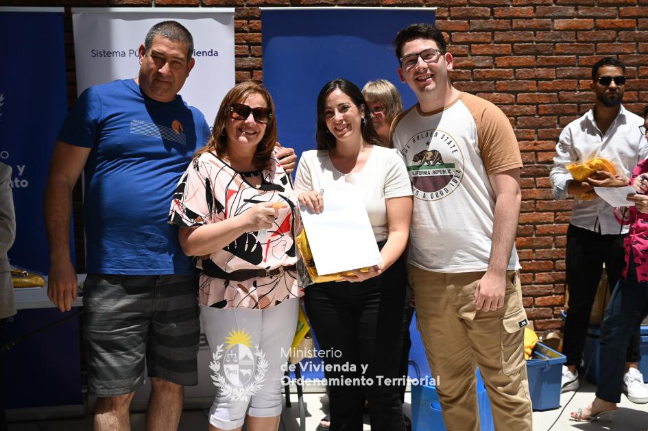 Familia recibiendo las llaves de su nueva casa familia posando junto a funcionaria después de recibir las llaves de su nuevo hogar