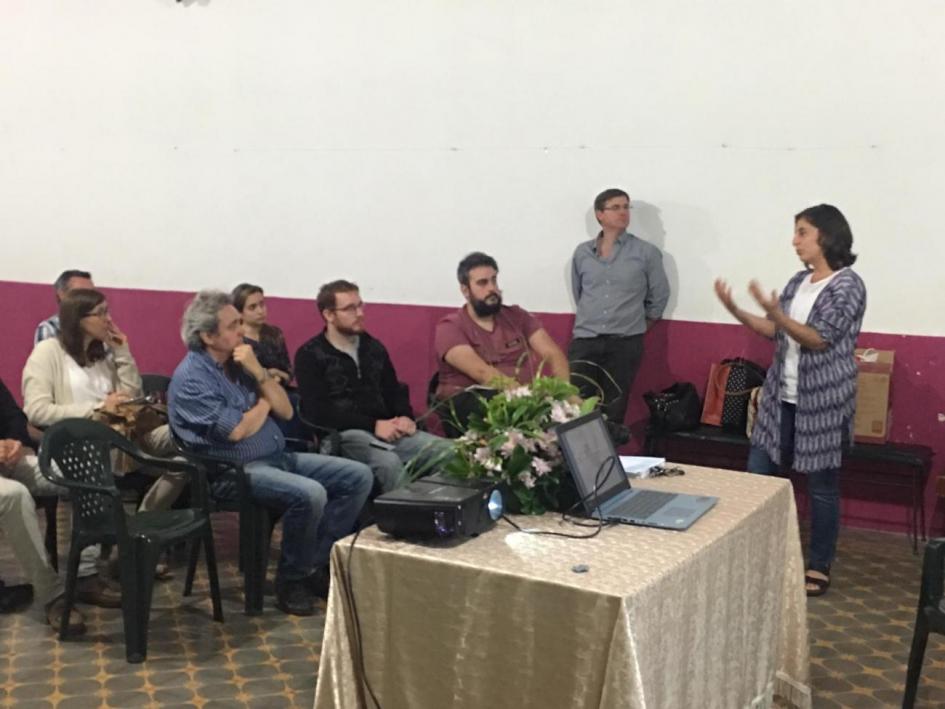 Técnica parada haciendo una presentación frente a grupo de personas que la escuchas sentadas en sus sillas