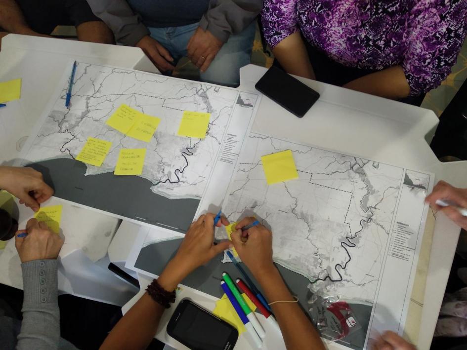 Juan Lacaze Una mesa con varios mapas, papeles adhesivos con escritura, marcadores, lapiceras y manos de varias personas