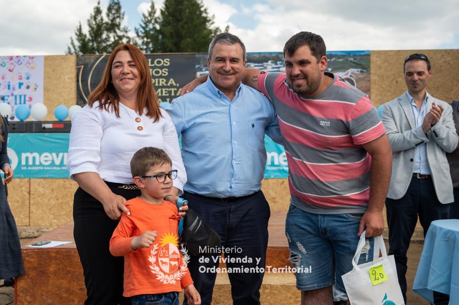 Ministro de vivienda posando sonriente junto a familia luego de entregarle las llaves de su vivienda