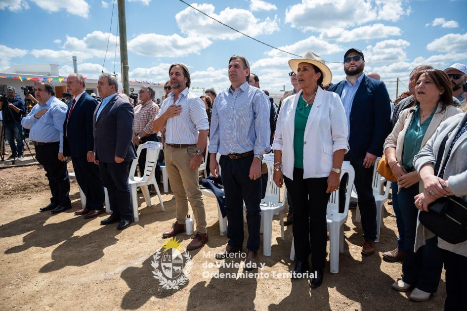 Diversas autoridades paradas juntas cantando el himno nacional 