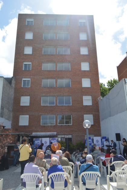 Edificio Fachada del edificio inaugurado y varios beneficiarios sentados al lado del parillero