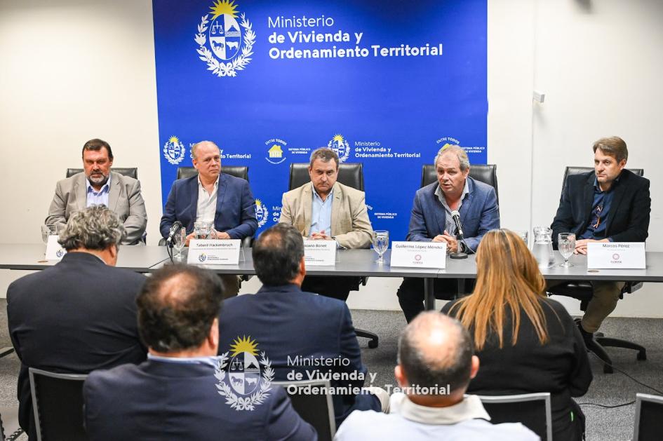 Ministro de vivienda sentado junto a las autoridades presentes mientras dan discurso