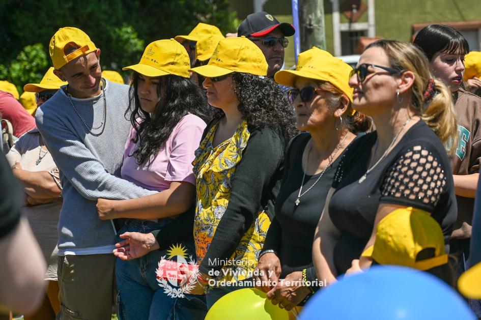 Vecinos presentes en la entrega de viviendas usando gorros del ministerio y abrazándose felizmente