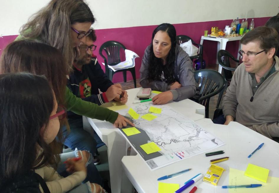 Juan Lacaze Taller con técnicos, vecinos y vecinas de la ciudad de Juan Lacaze. Sobre la mesa un mapa de la zona y papeles adhesivos. Alrededor de la mesa los participantes intercambiando.