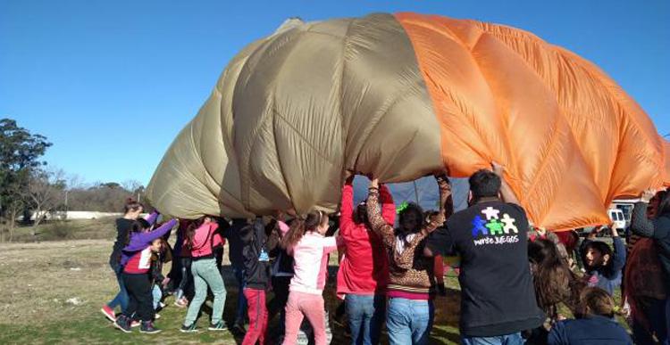 Fiesta infantil en barrio Lavalleja Varias personas sosteniendo una tela en forma de circulo grande con varios colores