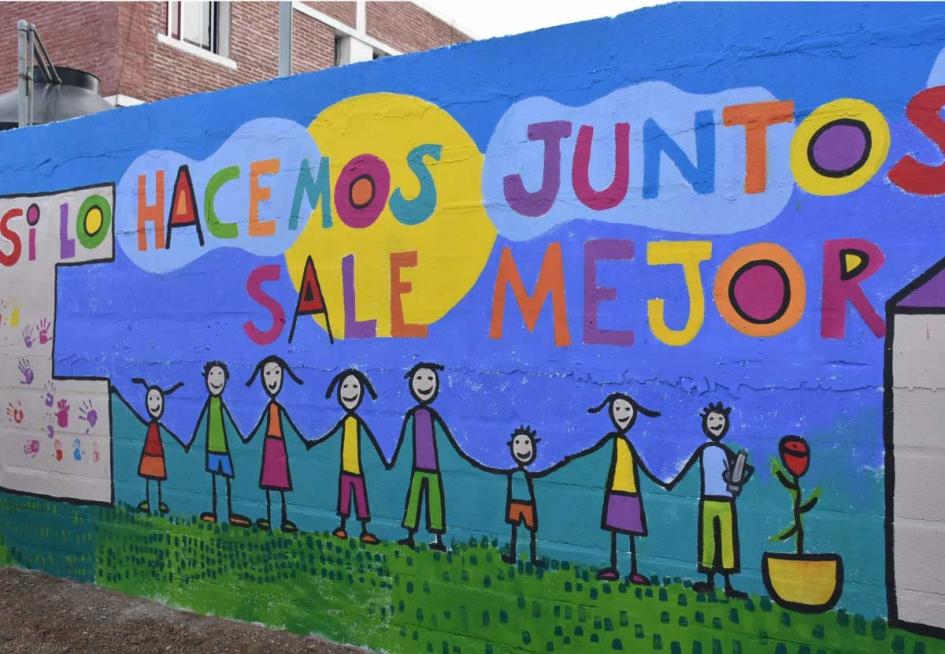 mural con la frase "si lo hacemos juntos lo hacemos mejor" y varias personas dibujadas tomas de la mano