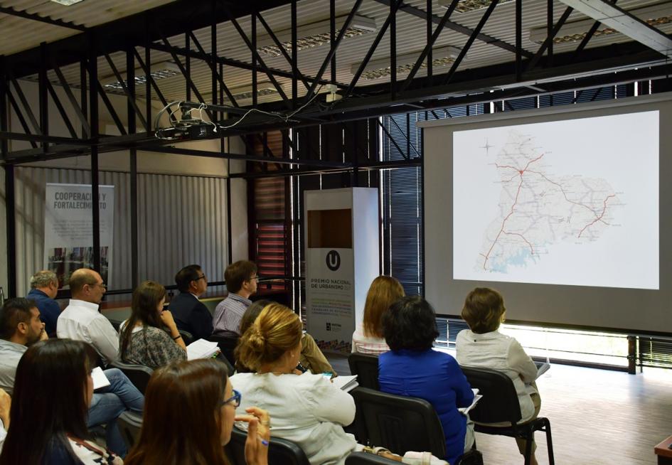 Presentación Plan Paso de los Toros En sala de reuniones de Dinot se encuentran el director nacional entrante Norbertino Suárez y el saliente José Freitas y más funcionarios de la Dinot sentados frente a una pantalla gigiante donde se observa un mapa, parte del contenido del Plan.