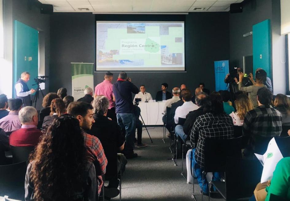 Presentación Programa Región Centro Se ve el publico de espaldas y al fondo en una mesa tipo panel autoridades con pantalla gigante de fondo con la imagen del programa. Autoridades de izquierda a derecha intendente de Durazno Carmelo Vidalín, subdirector de OPP Santiago Soto, el director de Descentralización e Inversión Pública de la OPP Pedro Apezteguía y el director nacional de Ordenamiento Territorial José Freitas