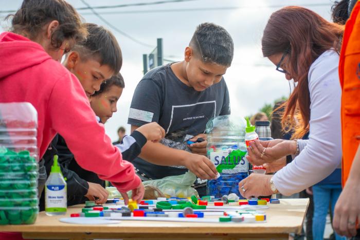 Niños armando cartel de fin de año con tapitas de refresco