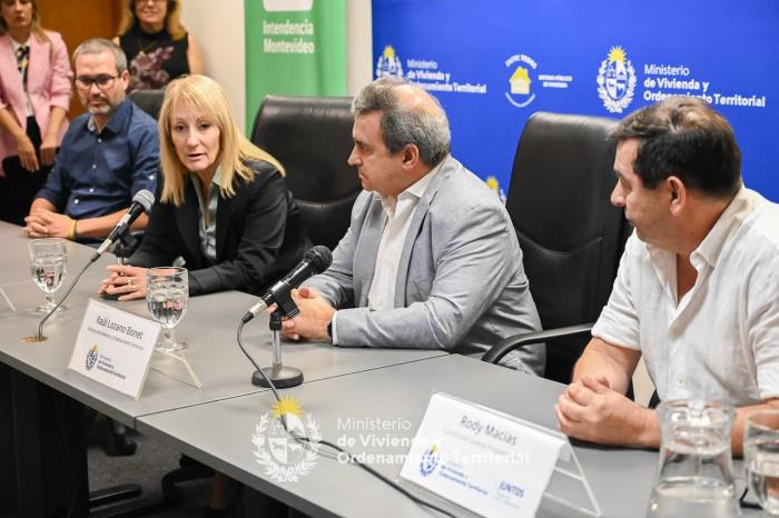 Carolina Cosse hablando al micrófono al lado de el Ministro de Vivienda y otras autoridades