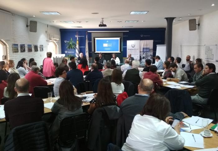 Imagen del teller con sala llena, varias mesas y un panel con el director nacional de Ordenamiento Territorial José Freitas y el director nacional de Descentralización de la OPP Pedro Apezteguía