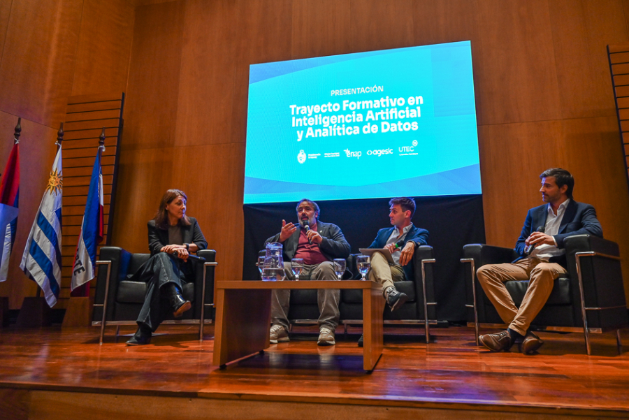 Cuatro participantes conversan sentados en sillones junto a una mesa, en un evento formal