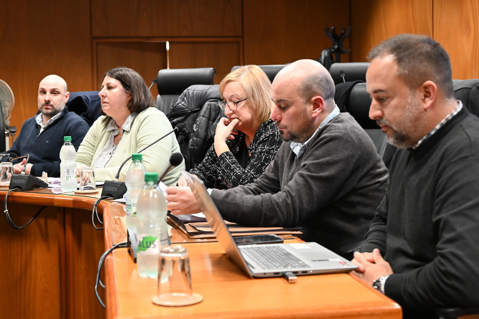Fotografía de una reunión formal con cinco personas sentadas en mesa de madera.