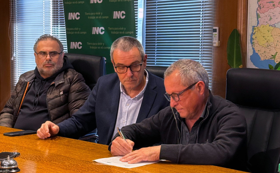 Presidente de Colonización, Alejandro Henry, firma el convenio en un escritorio. A su lado, lo observa el presidente de Inisa, Jaime Saavedra