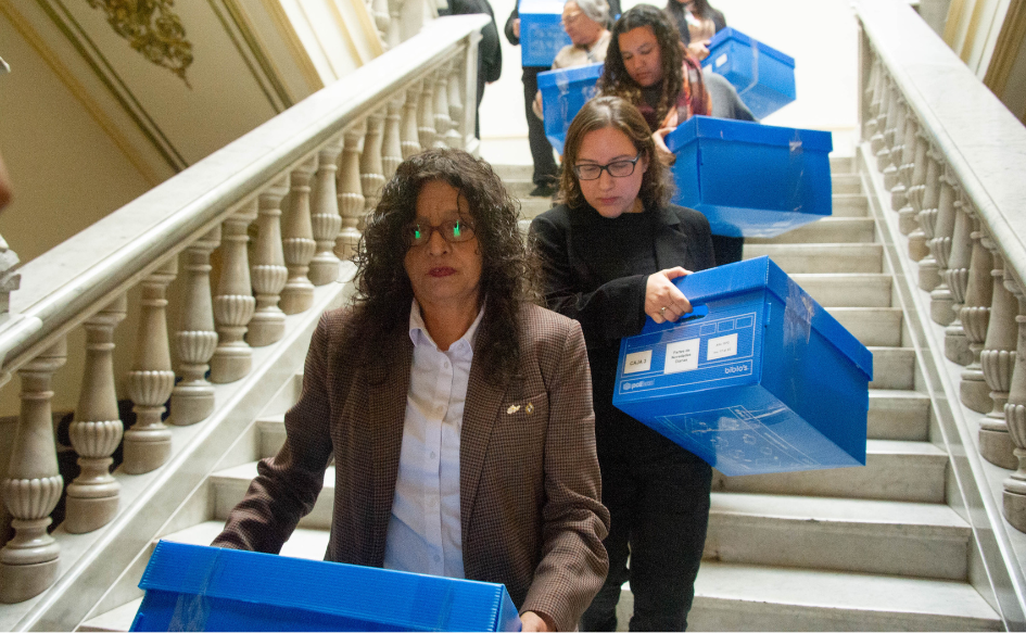 Directora de la Secretaría de Derechos Humanos para el Pasado Reciente, Alejandra Casablanca, encabeza una fila de personas que descienden por una escalera en la sede del Ministerio del Interior, cargando cajas.