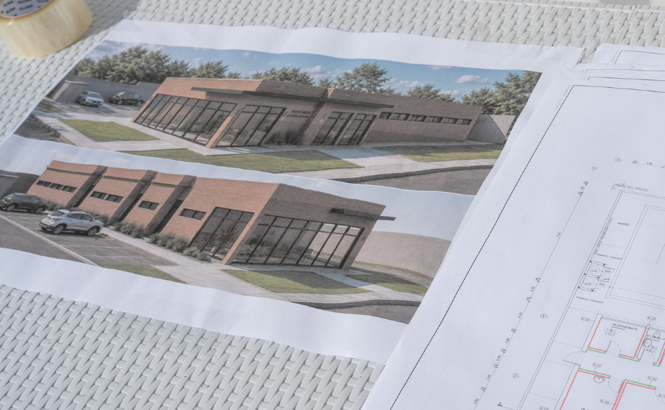 Render de la policlínica de Estación Atlántida apoyado sobre una mesa. A su lado, se ven trazos de los planos de la policlínica