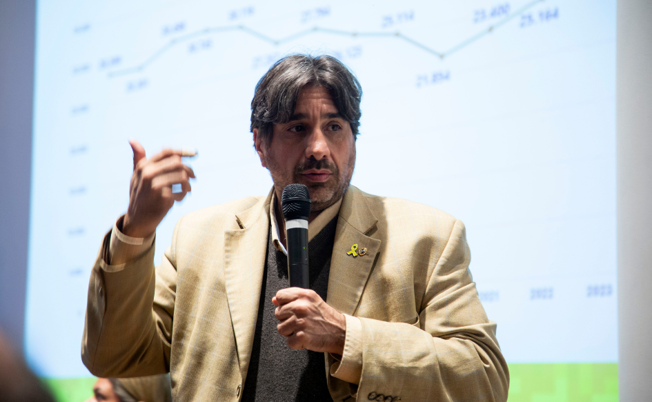 Presidente de Unasev, Marcelo Metediera, habla con un micrófono en la mano y una cinta amarilla en su solapa. Detrás, una gráfica que muestra una línea en ascenso