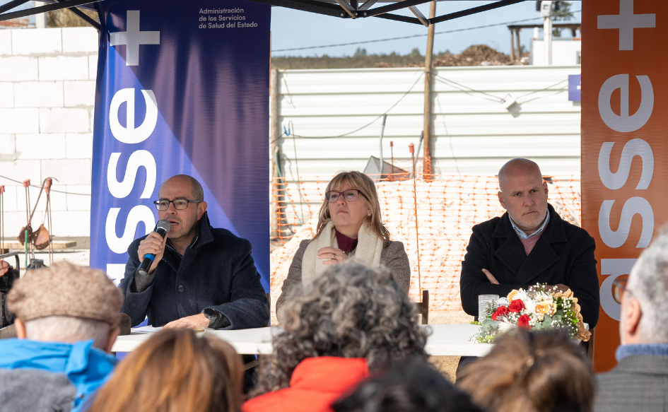 Presidente de ASSE, Álvaro Danza, habla con un micrófono de mano durante el lanzamiento de obras de la policlínica de Estación Atlántida. A su lado, lo escuchan la ministra de Salud Pública, Cristina Lustemberg, y el intendente de Canelones, Francisco Legnani. Detrás, las paredes que están siendo edificadas