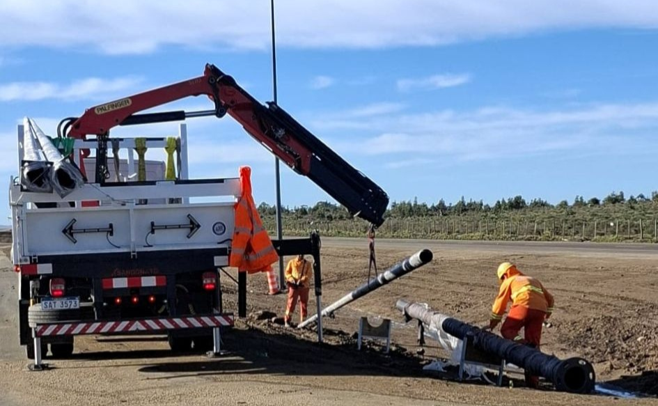 Dos obreros trabajan en la instalación de luminarias LED en ruta 9. En la ruta, un camión grúa eleva una columna.