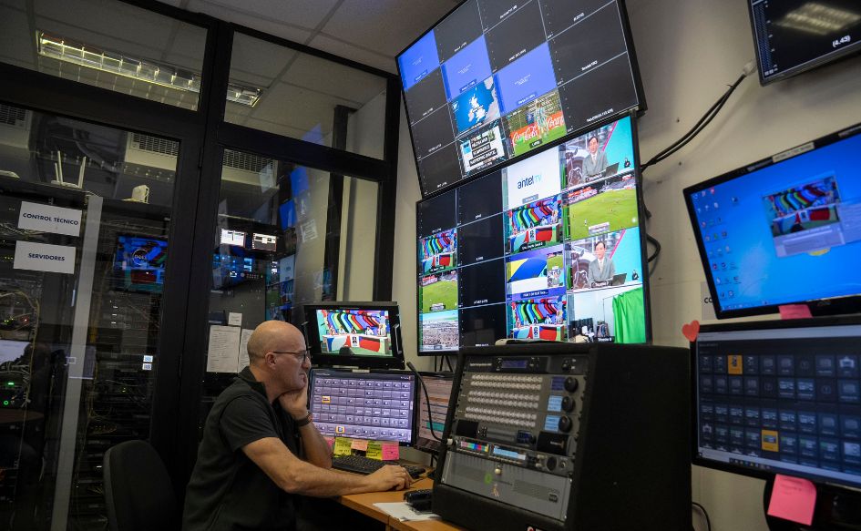 Hombre manipula un mouse en el centro de producción de contenidos del MIEM en el LATU. Alrededor, varios monitores reproducen imágenes del estudio y canchas de fútbol