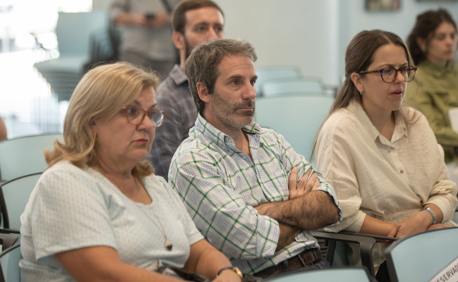 Hombre cruzado de brazos, observa a las autoridades desde el público