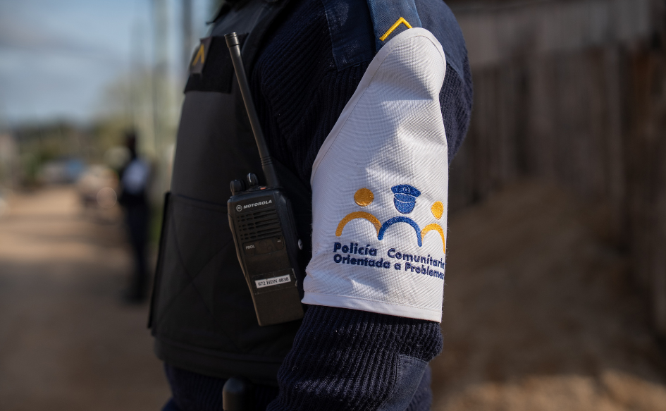 Un policía comunitario de pie, en una calle del barrio La Colina, durante el relevamiento de hogares del programa Más Barrio. Tiene un brazalete con el logo de la Policía Comunitaria Orientada a Problemas