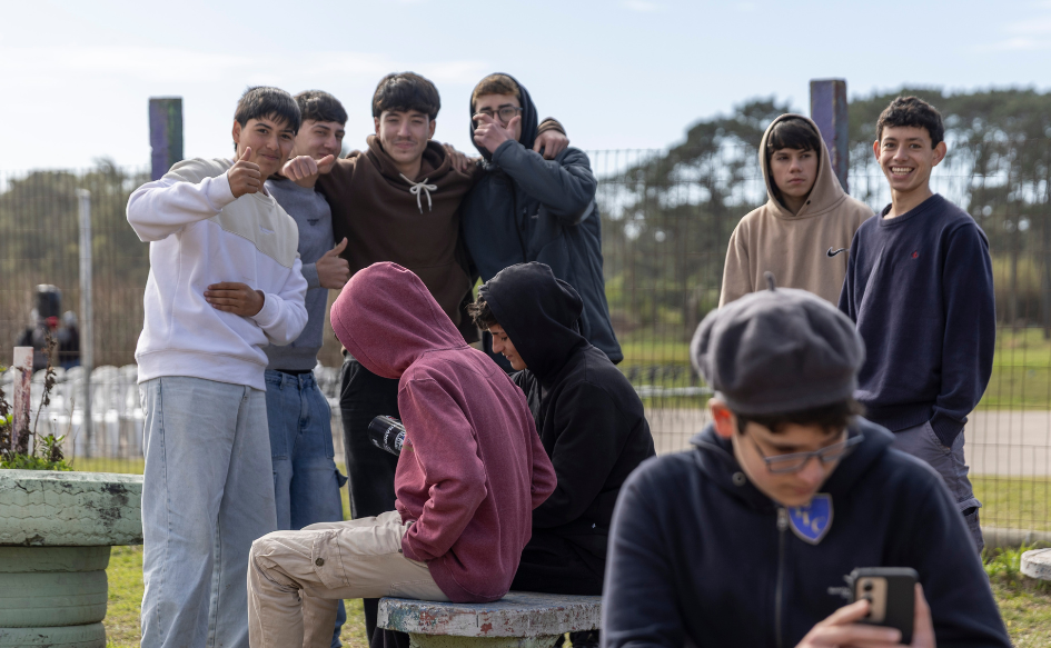 Cuatro estudiantes del liceo de La Coronilla miran a la cámara y levantan sus pulgares. Otros dos, sonríen. Delante de ellos, estudiantes sentados.