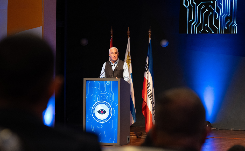 Ministro del Interior, Carlos Negro, en el escenario, habla de pie, detrás de un atril. Atrás de él, los pabellones patrios.