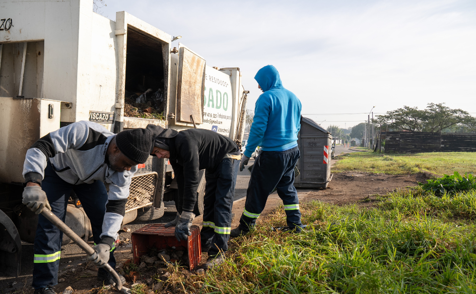 Dos funcionarios de la Intendencia de Montevideo juntan escombros en un predio de Cerro Norte. Detrás de ellos, un camión donde depositan lo recolectado.