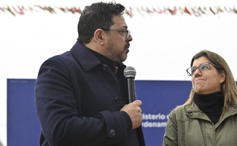 Secretario de Presidencia. Alejandro Sánchez, habla de pie, con un micro´fono en la mano, frente al tanque de agua que caracterizaba al asentamiento. A su lado, la ministra de Vivienda, Tamara Paseyro, lo observa atentamente