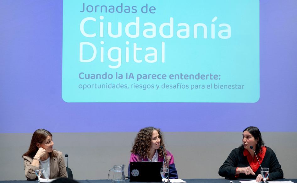Consejera de ANEP, Carolina Pallas, habla durante la apertura de las Jornadas de Ciudadanía Digital 2026. A su lado, la escuchan sonrientes la directora de Sociedad de la Información de Agesic, Virginia Pardo, y la presidenta de Ceibal, Fiorella Haim. En el fondo, se proyecta la frase "Jornadas de Ciudadanía Digital. Cuando la IA parece entenderte: oportunidades, riesgos y desafíos para el bienestar"