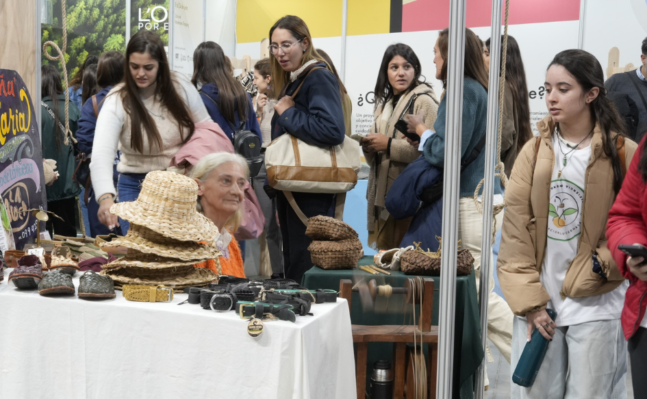 Varias mujeres observan sombreros, alpargatas y cintos dispuestos sobre la mesa de un stand en la Expo Uruguay Sostenible
